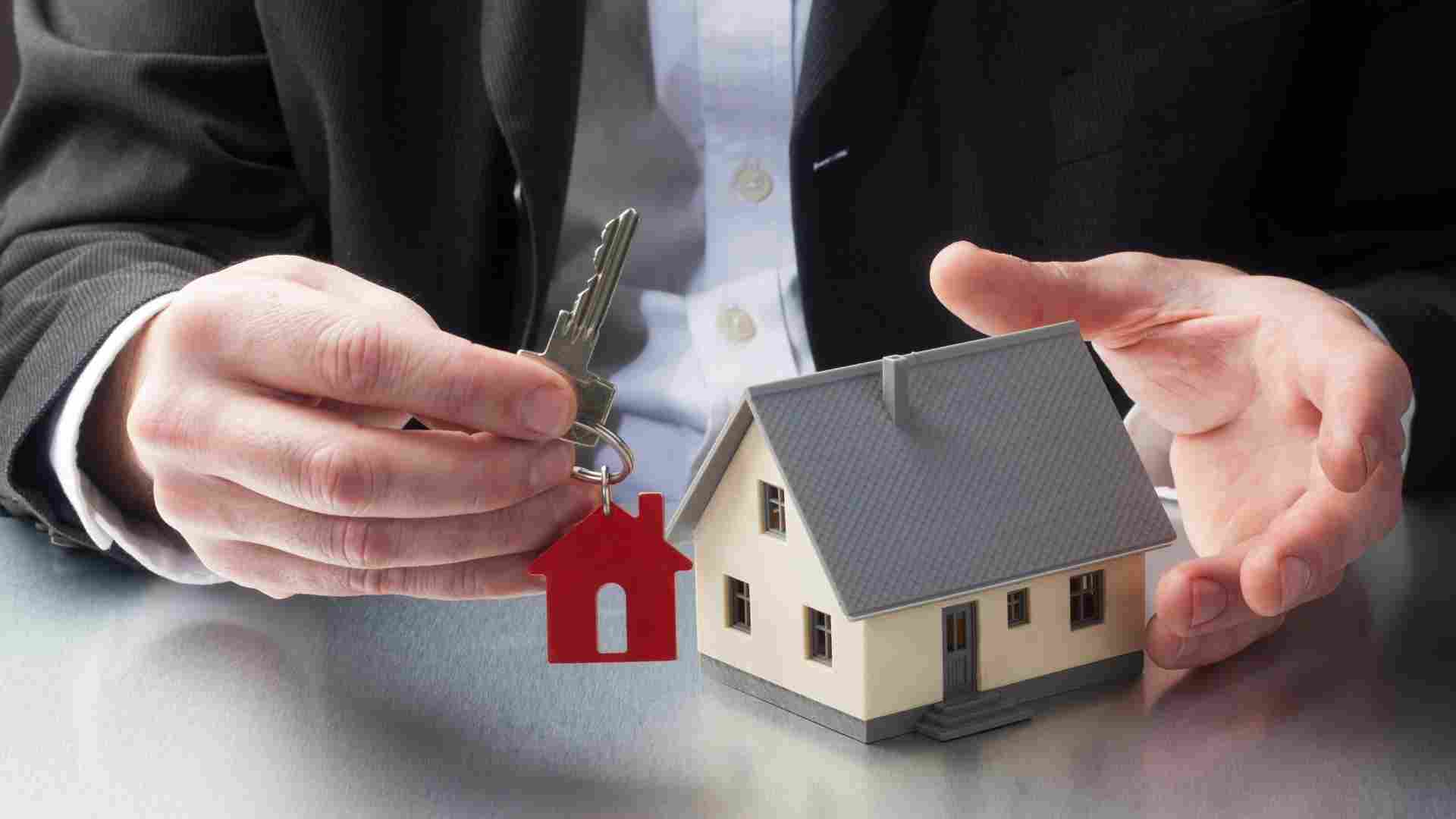 person holding a set of keys next to a house figurine