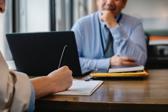 person signing a document while sitting across from someone