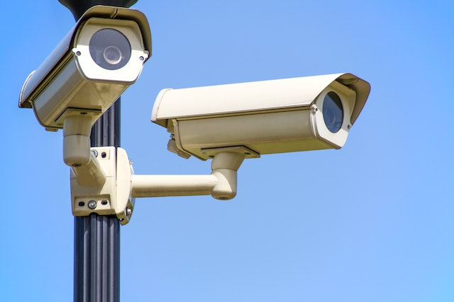 two security cameras on a large post against a blue sky